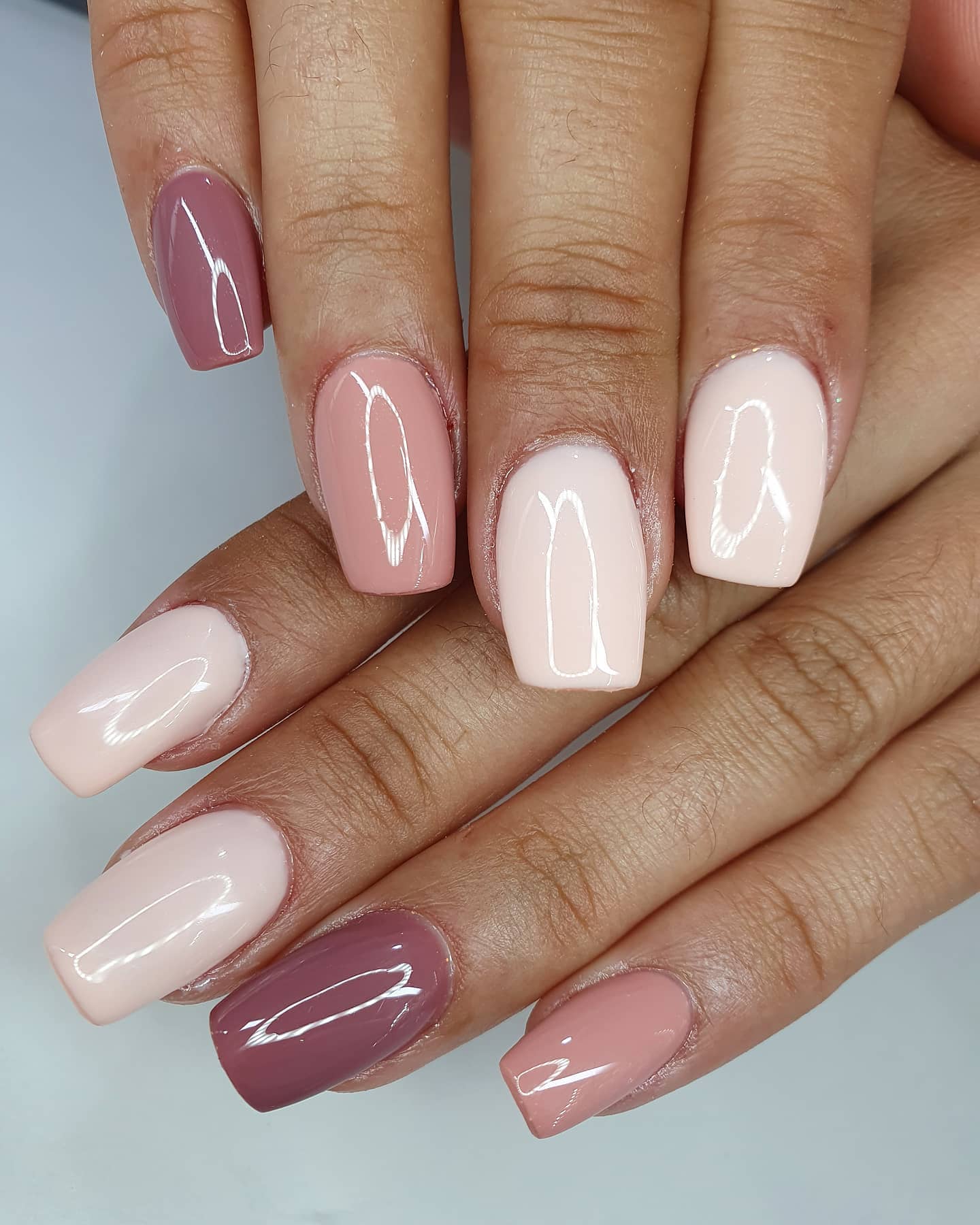 Manicura en cinco tonos nude, rosa y malva sobre uñas cuadradas, en la mesa blanca de Mona.gy